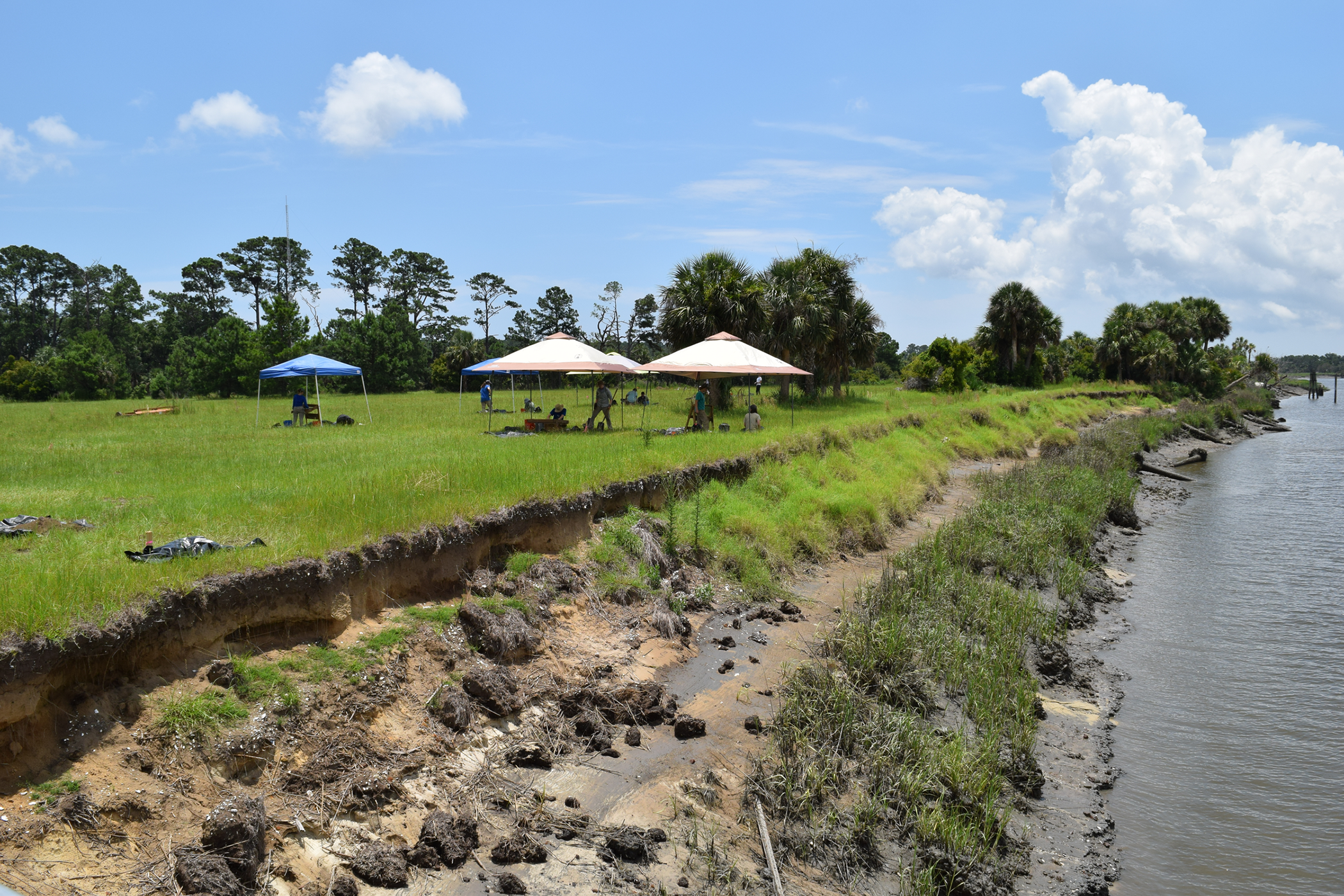 photo of shoreline, with grass, tents, and water, day