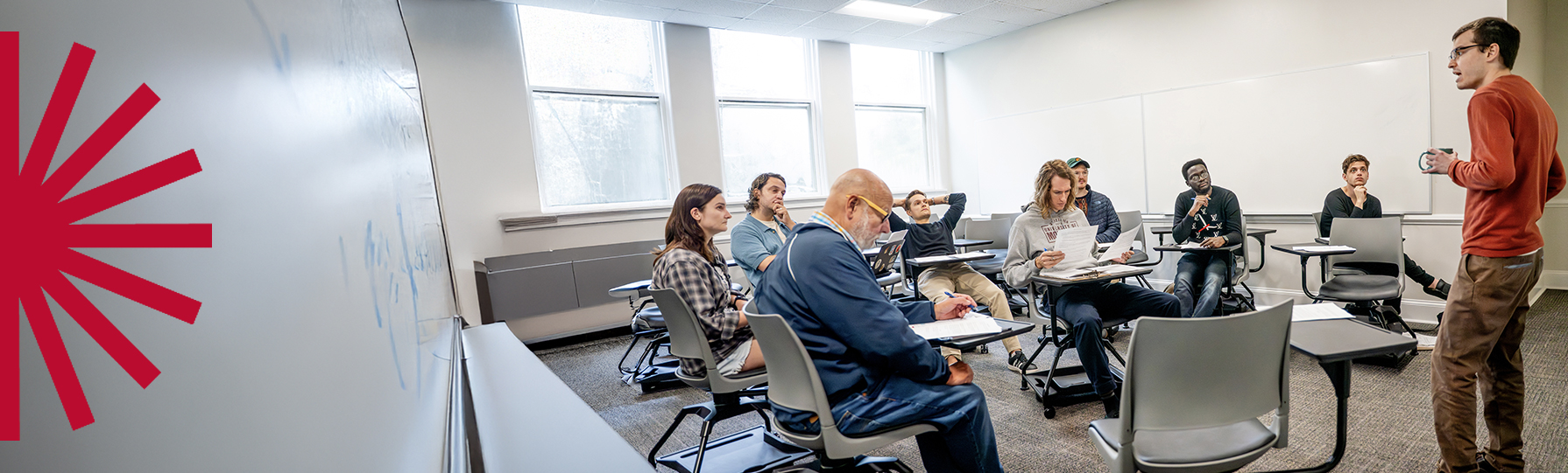Man holding a coffee cup, speaking to a group of students