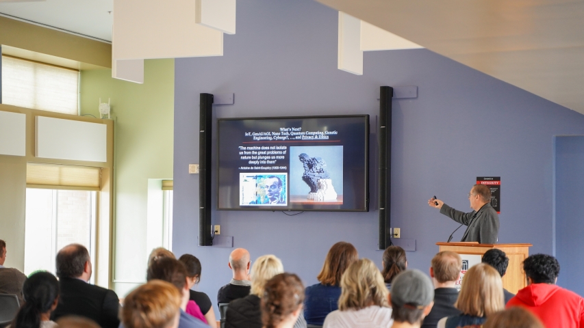 photo of man speaking, with screen, audience