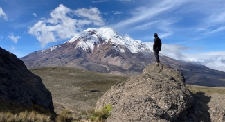 photo of man standing on rock looking at mountain, day