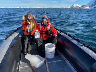 photo of two people in a small boat in water, snow-capped land in background