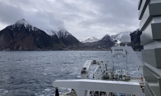 photo of shoreline mountain with clouds, sea and ship in foreground