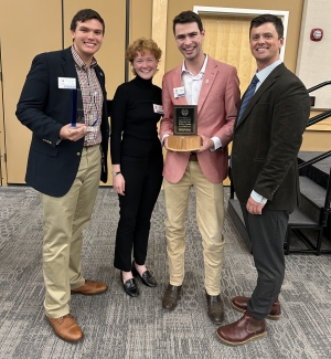 photo of four people, one holding a trophy