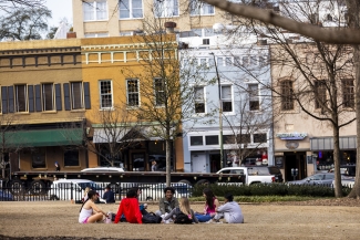 photo of people sitting in grass, day, downtown in background