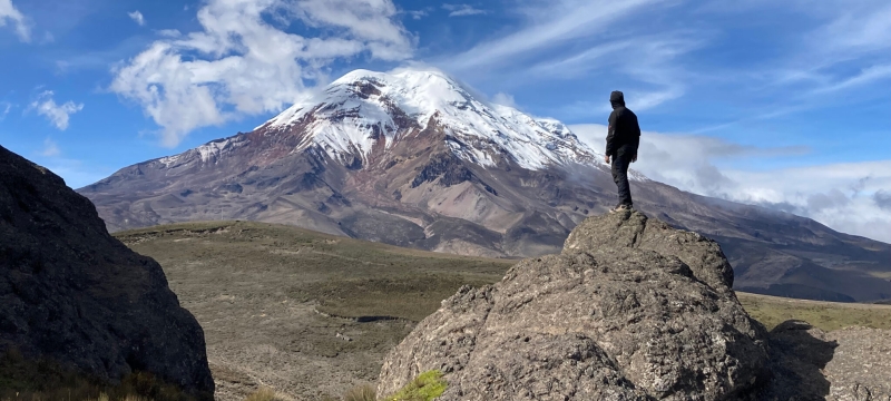photo of man standing on rock looking at mountain, day