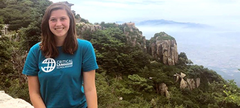 woman sitting on wall, with sky and mountain 