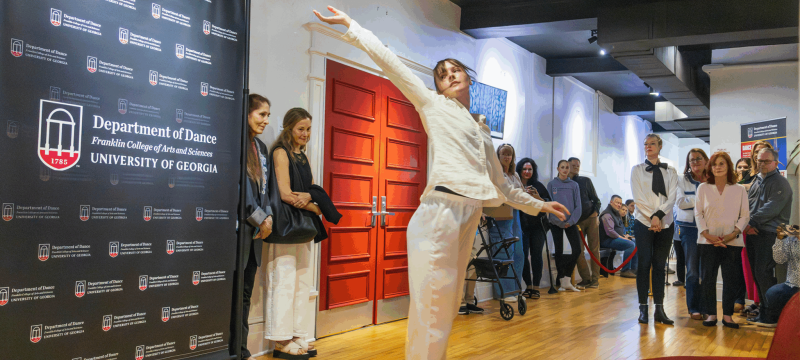 woman dances in room, people and banner in background.