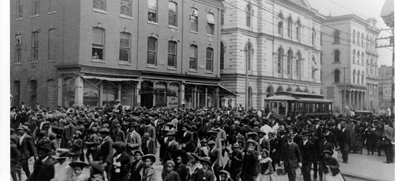 black and white photo of people in the street, with buildings