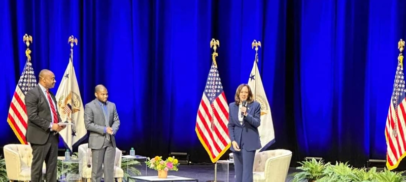 photo of three people on stage, with flags and chairs