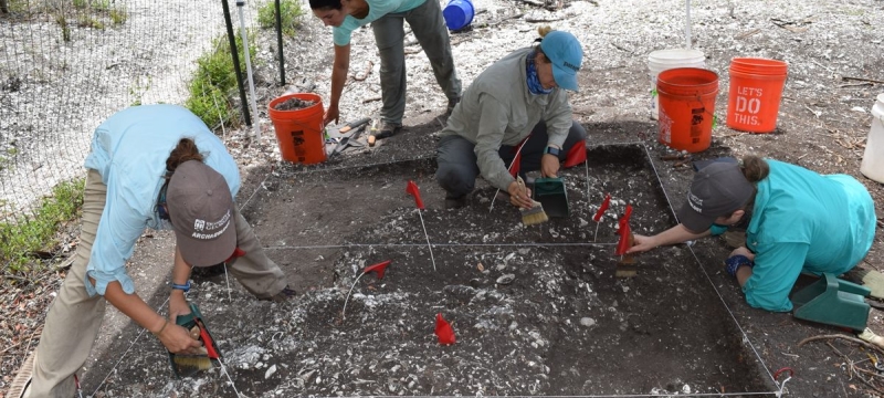photo of four people on archeological dig, with trowels, brushes and buckets