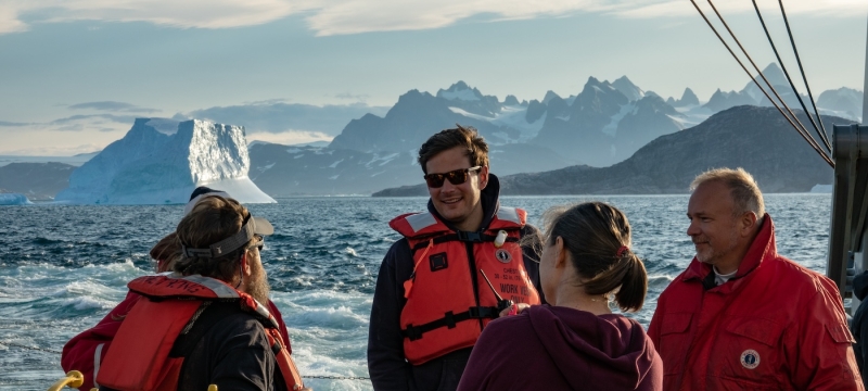 photo of people on ship, mountains in background, day