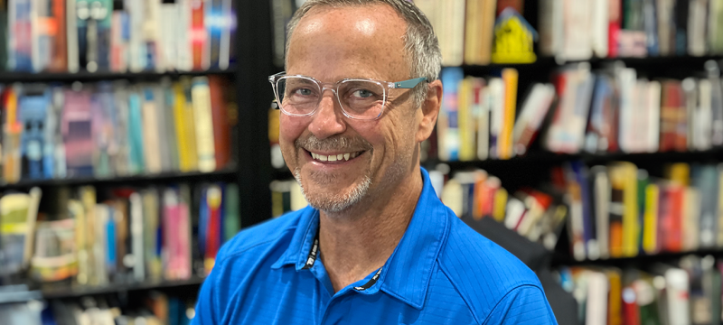 photo of man, bookshelves and books in background