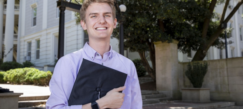 photo of man with cap standing in front of arch 