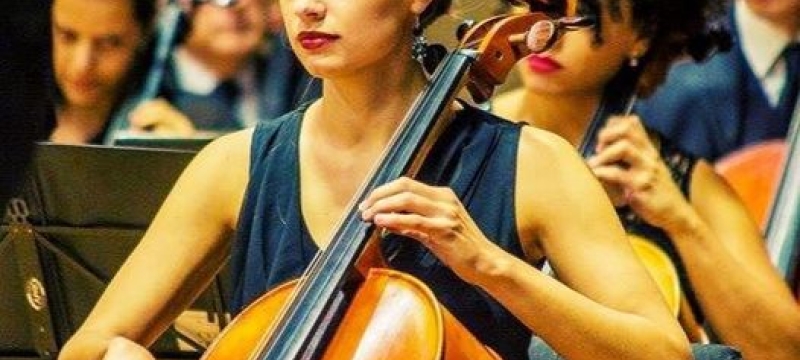 photo of woman playing cello, with other performers in background