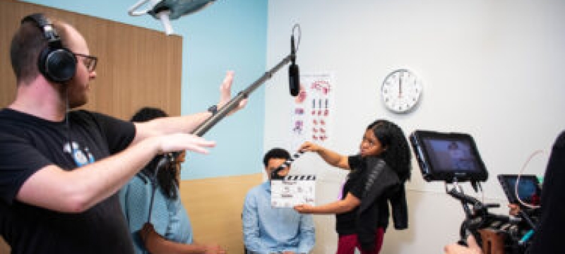 photo of film shoot, with clapper board, people, microphone on boom stand
