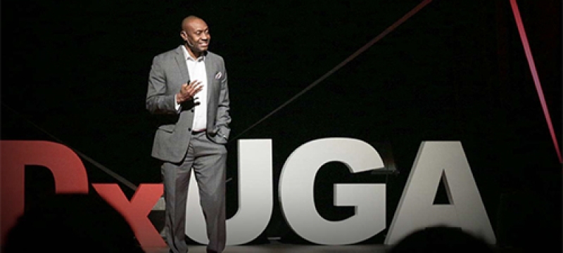 photo of man on stage talking to an audience in foreground