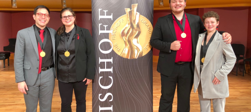 photo of four people with medals and banner in performance hall