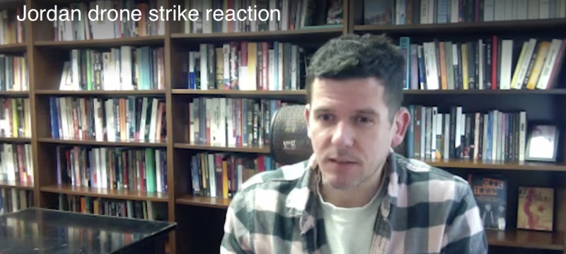 still photo of man, with bookshelves in background