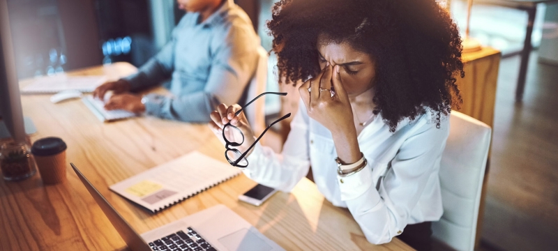 photo of two people on computers, woman in foreground holding glasses