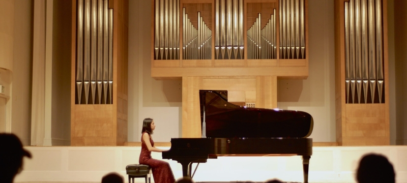 photo of woman in piano performance, with audience silhouette foreground