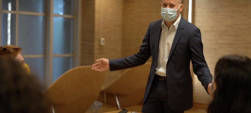 photo of man with mask standing at table, arms spread