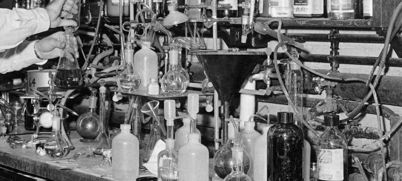black white photo of beakers and test tubes, arms of a man
