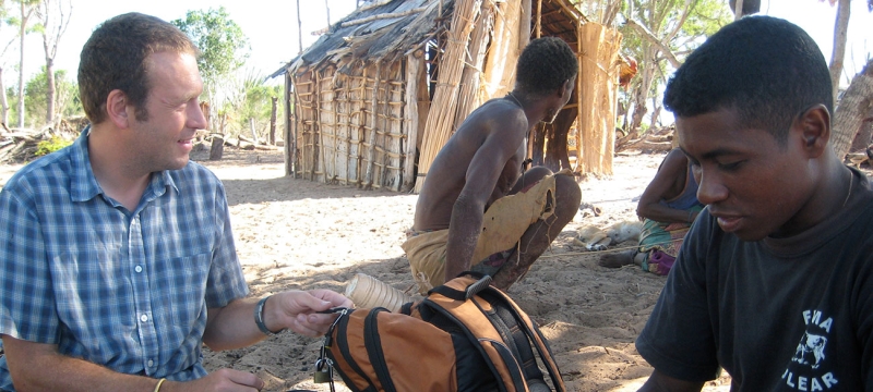 photo of three men with hut in background, day