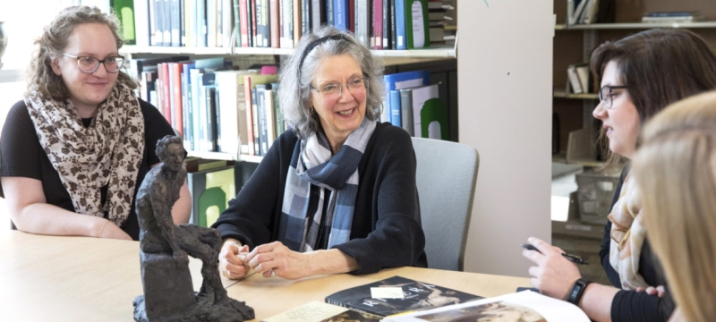 photo of four women sitting at a table with a small sculpture