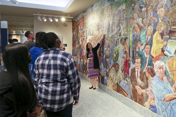 photo of students, with mural and woman pointing