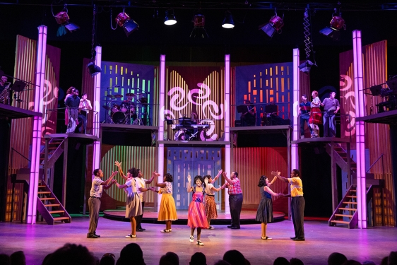 photo of stage play play production with people, lighted columns and steps