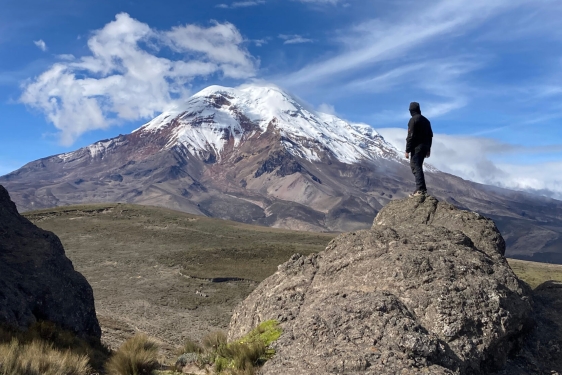 photo of man standing on rock looking at mountain, day