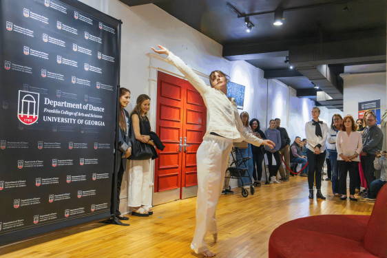 woman dances in room, people and banner in background.