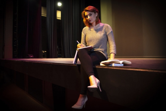 photo of woman sitting on stage with book and pen