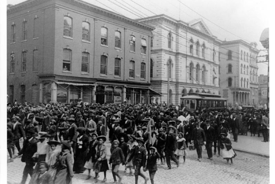 black and white photo of people in the street, with buildings