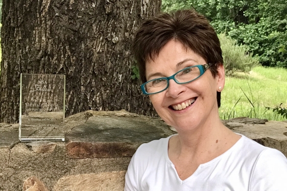 photo of woman outdoors with rock wall and glass plaque