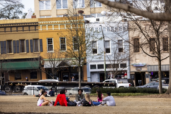 photo of people sitting in grass, day, downtown in background