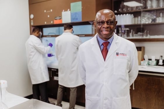 photo of man in lab coat, with two other men in background lab
