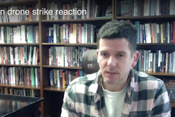still photo of man, with bookshelves in background