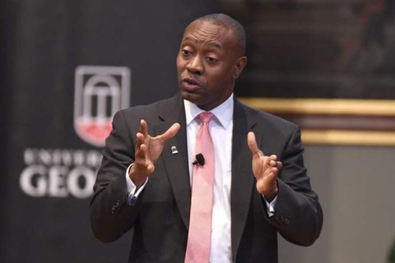 photo of man speaking, with banner in background 