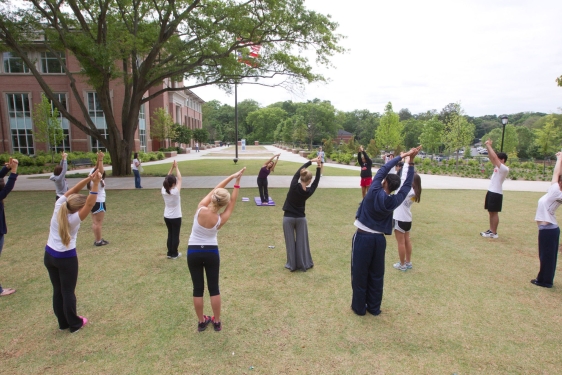 photo of group of people stretching with arms overhead, outdoors