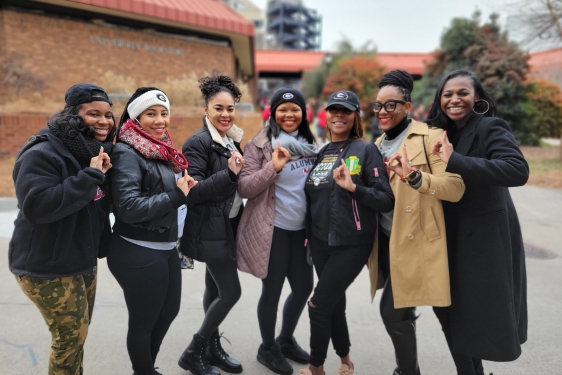 photo of seven women outdoors, with stadium in background