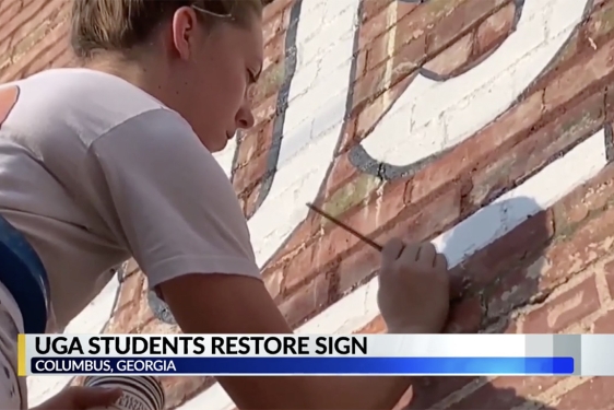 photo of woman painting letters on exterior brick wall