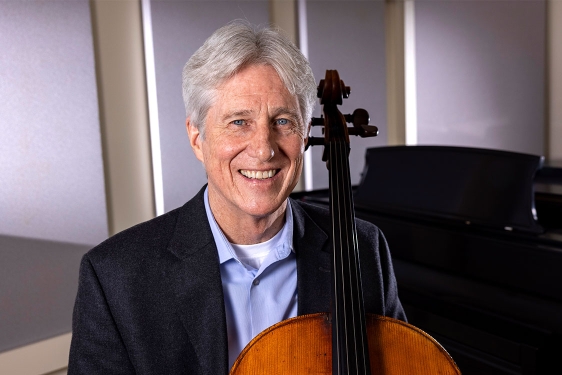 photo of man with cello, piano in background