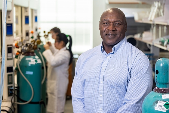 photo of man in lab, with people in lab coats, equipment in background