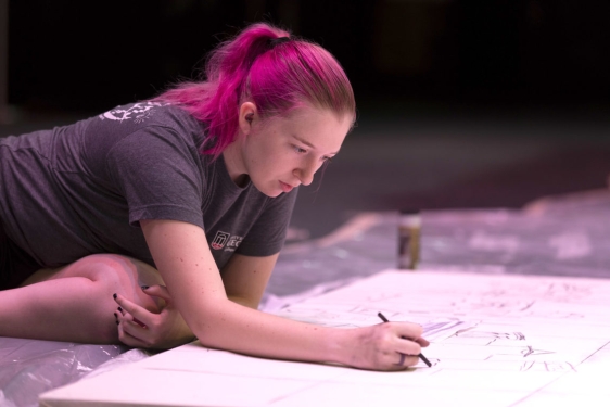 photo of woman leaning over a large drawing surface with pencils