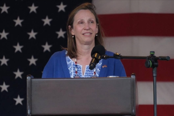 photo of woman at podium, American flag in background